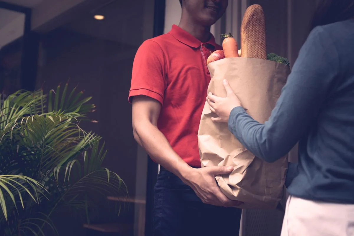 A grocery bag being handed over at a doorway